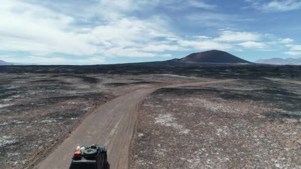 Scena aerea del furgone 4x4 che guida fuori strada tra letti di lava, lapilli neri. Vulcano scuro cono CarachiPampa sullo sfondo. Paesaggio arido mistico. Catamarca, Argentina — Video Stock