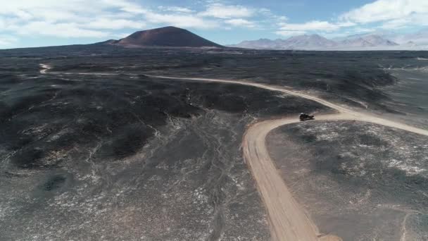 4x4 远征面包车在熔岩床、黑色拉皮利斯之间的道路上行驶的空中场景。黑暗火山卡拉切帕帕锥在背景。多神贫瘠的景观。阿根廷卡塔马卡 — 图库视频影像