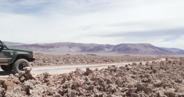 Camioneta 4x4 que viaja fuera de la carretera en el campo de sal sucio. Paisaje desértico con montañas de colores al fondo. Antofagasta de la sierra, Catamarca, Argentina — Vídeo de stock