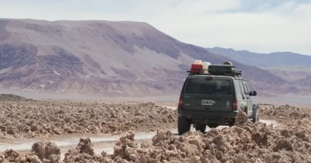 Camioneta 4x4 que viaja fuera de la carretera en el campo de sal sucio. Paisaje desértico con montañas de colores al fondo. Antofagasta de la sierra, Catamarca, Argentina — Vídeo de stock