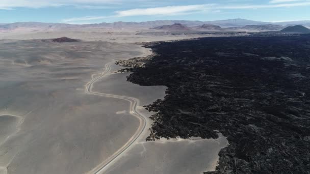 Voando no limite do leito negro de lava e deserto com estrada. Texturas vulcânicas naturais, padrões. fundo de montanhas e deserto. Antofagasta de la Sierra, Catamarca, Argentina — Vídeo de Stock