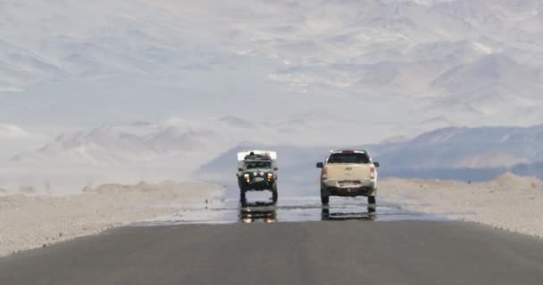 Escena fija de furgoneta 4x4 con caravana que viaja por carretera con efecto de neblina de calor en el desierto y la región seca montañosa. Ilusión de vapor de agua. Mirage. Antofagasta de la Sierra, Catamarca, Argentina — Vídeo de stock