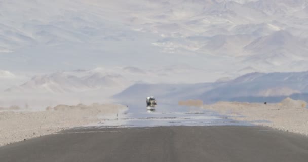 Scena tranquilla di furgone 4x4 con carovana che viaggia su strada con effetto caldo foschia nel deserto e nella regione montuosa asciutta. L'ilusione del vapore acqueo. Miraggio. Antofagasta de la Sierra, Catamarca, Argentina — Video Stock