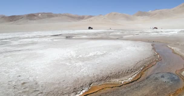 Wandelen langs de hete meandrischgetal-rivier met waterdamp Oplopend. 4x4 bestelwagens op de achtergrond. Volcan galan Expedition, Antofagasta de la Sierra, Catamarca, Argentinië — Stockvideo