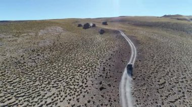4 x 4 van, parkur otlar ve yaşlı kayalar ile yüksek dağın altın manzaraya yoldan sürüş hava dron sahne. Galan volkan gezi, Antofagasta de la Sierra, Catamarca, Argentina.