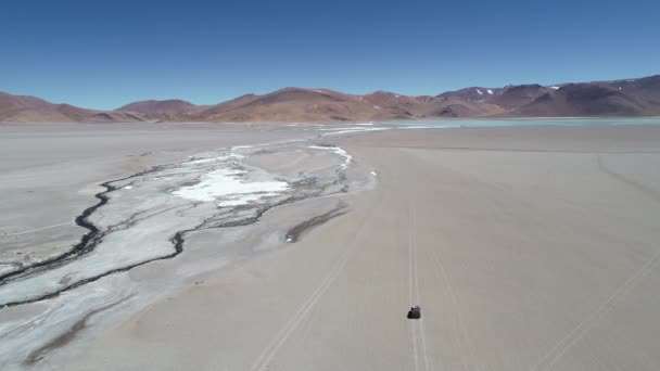Légi drone jelenet 4 x 4 van vezetés off road, fehér forró folyó mellett. Kék Diamante lagúna Galan vulkán kráterében háttér. Csökkenő közelében autó. Antofagasta de la Sierra, Catamarca, Argentína — Stock videók