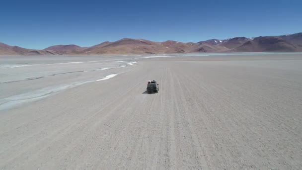 Escena aérea que sigue por la espalda y pasa cerca de furgoneta que conduce fuera de la carretera junto al río caliente blanco. Laguna Diamante Azul en el cráter Volcán Galán al fondo. Antofagasta de la Sierra — Vídeos de Stock