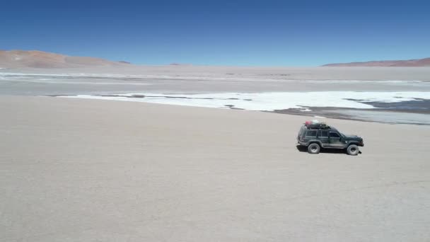 Escena aérea del dron siguiendo furgoneta 4x4 desde el lado que conduce fuera de la carretera junto al río salado en el paisaje desértico en el cráter del volcán Galán. Excursión en Antofagasta de la Sierra, Catamarca Argentina — Vídeo de stock