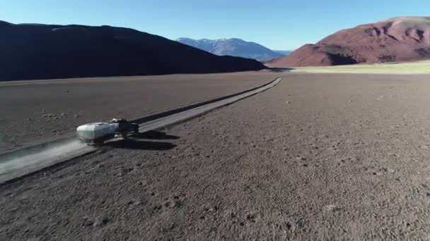 Escena aérea de drones de 4x4 con caravana que viaja fuera de la carretera en pista de grava en montañas desérticas. Siguiendo el coche desde el costado. Andes al fondo. Antofalla, Catamarca, Argentina — Vídeos de Stock