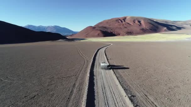 Scène aérienne de drone de van avec caravane voyageant hors route sur une piste de gravier sur des montagnes désertiques. Suivre la voiture par derrière voler sur la voiture. Andes à l'arrière-plan. Antofalla — Video