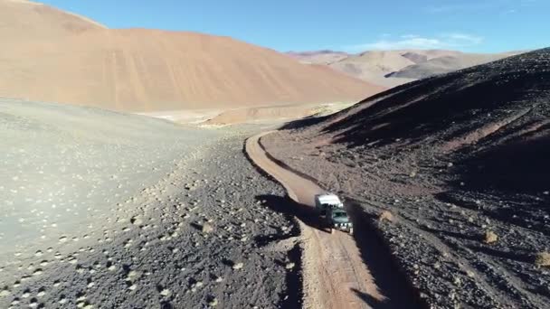 Drohnen-Szene eines Geländewagens mit Wohnwagen, der bei Sonnenuntergang auf einem Schotterweg in den einsamen Bergen unterwegs ist. nachfolgendes Auto von vorne. antofalla, catamarca, argentina — Stockvideo