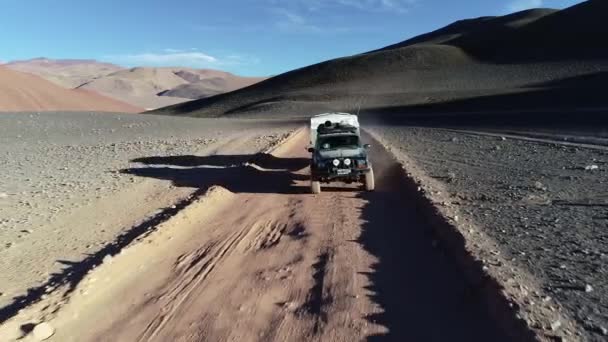 Antena po z przodu van ekspedycyjny z przyczepą kempingową podróżujących Off Road na torze żwirowym na pustynie Colorfull gór o zachodzie słońca. Antofalla, Catamarca, Argentyna — Wideo stockowe