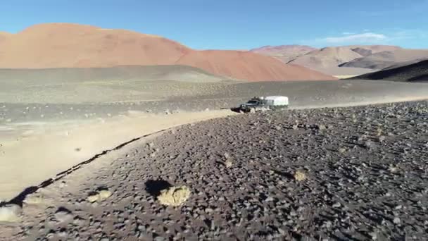 석양이 질 무렵 사막의 색이 찬 산의 자갈 길에서 카라반이 도로를 벗어나는 원정 밴을 타고 공중을 따라갑니다. 안토팔라, 카타마르카, 아르헨티나 — 비디오