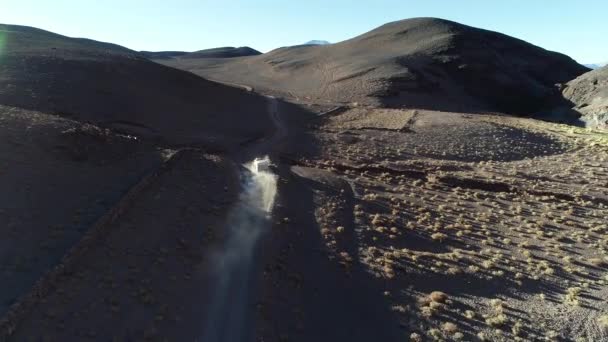 Gün batımında çöldağlarında çakıl yolda yoldan çıkan kervanlı bir keşif minibüsü ön taraftan takip edin. Antofalla, Catamarca, Arjantin — Stok video