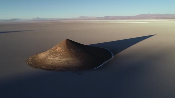 Aerial general view of natural isolated pyamid in wide brown and white salar at sunset. Golden hour. Abstract nature. Big shadow of cone. Cono de Arita, Salta, Argentina. — Stock Video