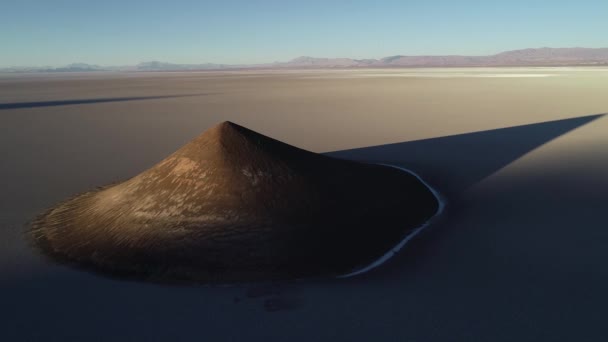 Aerial general view of natural isolated pyamid in wide brown and white salar at sunset. Flying backwards. Golden hour. Abstract nature. Big shadow of cone. Cono de Arita, Salta, Argentina. — Stock Video
