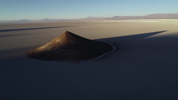 Vue aérienne générale du pyamide naturel isolé dans un large salar brun et blanc au coucher du soleil. Voler à reculons. L'heure dorée. Nature abstraite. Grosse ombre de cône. Cono de Arita, Salta, Argentine .
