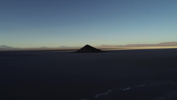 Visão geral aérea da pirâmide isolada natural em amplo salar marrom e branco ao pôr do sol, cone na sombra. Descendo sobre o deserto branco. Hora de ouro. Natureza abstracta. Cono de Arita, Salta, Argentina — Vídeo de Stock