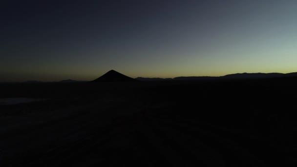 Сцена воздушного беспилотника с силуэтом гор и естественным идеальным пирамидом на восходе солнца. Черно-оранжевая сцена. Salar de Arizaro, Cono de arita, Сальта, Аргентина — стоковое видео