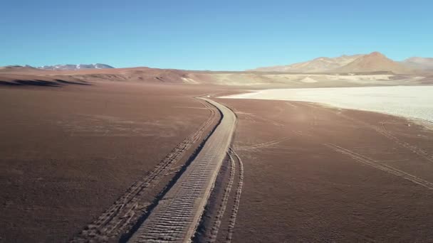 Escena aérea de aviones no tripulados volando fuera de la pista de carretera en el límite con el desierto y el paisaje salar. Marrón erosionó montañas. Arizaro salar, Salta, Argentina — Vídeo de stock