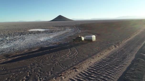 Cena aérea drone voando paraguerras 4x4 off van estrada com caravana no limite de salar branco com montanhas desertas marrons. A passar perto do casco. Pôr do sol. Salar de Arizaro, Salta, Argentina — Vídeo de Stock