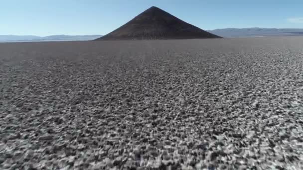 Escena aérea que vuela rápidamente ascendiendo a lo largo del salar hacia la piramida aislada natural en amplio salar marrón y blanco. Vista general del Cono de Arita, Salta, Argentina . — Vídeo de stock