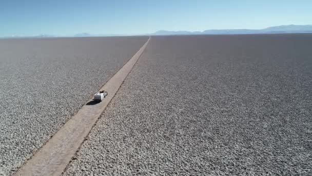 Εναέρια αεροκατευθυνόμενα σκηνή 4x4 με τροχόσπιτο που ταξιδεύει κατά μήκος λευκό πλατύ salar με. Από τις λεπτομέρειες του αυτοκινήτου πάνω από την οδική τροχιά ανεβαίνει σε γενική όψη του τοπίου. Αριάρο Σαλάρ, Σάλτα, Αργεντινή — Αρχείο Βίντεο