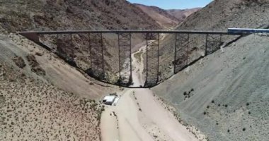 Çölgibi dağlık arazide eski metal köprüden geçen trenin havadan insansız hava aracı sahnesi. Couds Treni, tren de las nubes, San Antonio de los Cobres, Salta, Arjantin.