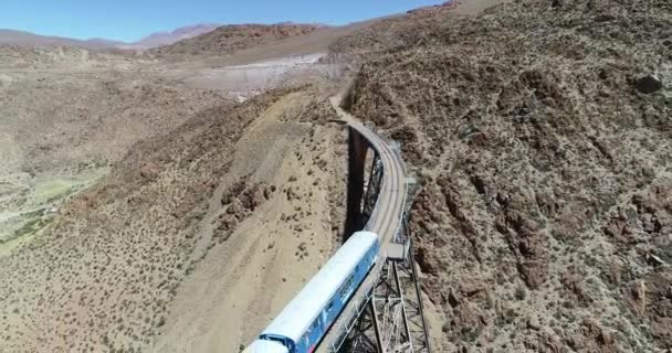 Vuelo aéreo sobre el tren mientras conduce a través de un viejo puente metálico en un paisaje montañoso desértico. Vista general del puente de hierro. Tren de los couds, tren de las nubes, San Antonio de los Cobres — Vídeos de Stock