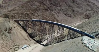 Terki dağlık arazide eski metal köprüden geçerken havadan yaklaşan tren. Demir köprünün genel görünümü. Couds Treni, tren de las nubes, San Antonio de los Cobres