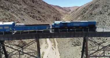 Çölgibi dağlık vadide eski metal köprüden geçen vagon ve lokomotif treninin açık çekimine kadar havadan. Couds Treni, tren de las nubes, San Antonio de los Cobres