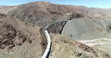 Terki dağlık arazide eski metal köprüden geçerken trenin üzerinden hava uçuşu. Demir köprünün genel görünümü. Couds Treni, tren de las nubes, San Antonio de los Cobres