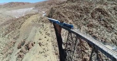 Terki dağlık arazide eski metal köprüden geçerken trenin etrafında uçan havadan. Demir köprünün genel görünümü. Couds Treni, tren de las nubes, San Antonio de los Cobres