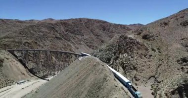 Çölgibi dağlık vadide eski metal köprü üzerinden sürüş tren havadan drone sahne. Demir köprünün genel görünümü. Couds Treni, tren de las nubes, San Antonio de los Cobres