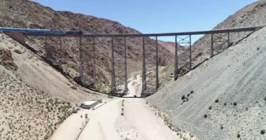 Çölgibi dağlık vadide eski metal köprü üzerinden sürüş tren havadan drone sahne. Demir köprünün genel görünümü. Couds Treni, tren de las nubes, San Antonio de los Cobres