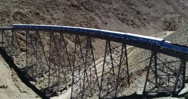 Aerial approaching from front to senital view to train while it drives through old metal bridge at desertic mountainous landscape. Train of the couds, tren de las nubes, San Antonio de los Cobres — Stock Video