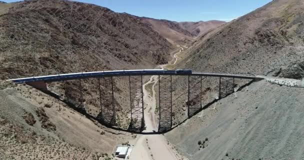 Aerial approaching train while it drives through old metal bridge at desertic mountainous landscape. General view of iron bridge. Train of the couds, tren de las nubes, San Antonio de los Cobres — Stock Video