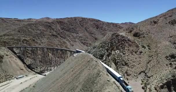 Escena aérea del dron del tren que conduce a través del viejo puente metálico en el valle montañoso desértico. Vista general del puente de hierro. Tren de los couds, tren de las nubes, San Antonio de los Cobres — Vídeos de Stock