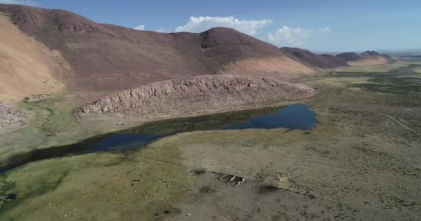 Cena de drones aéreos voando em direção a ruínas de casas em paisagem seca com dunas, colinas rochosas e pouco oásis. Abra Pampa, jujuy, Argentina — Vídeo de Stock