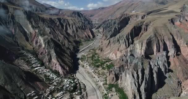 Vuelo aéreo sobre Iruya, ciudad escondida, en el valle estrecho empinado rodeado de bosques y colinas secas de colores en el fondo. Población turística de Salta, Argentina — Vídeo de stock