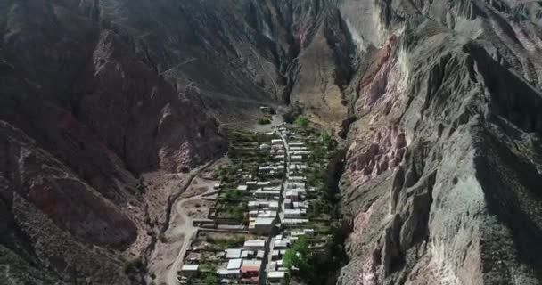 Voar aéreo sobre Iruya, cidade escondida, em vale estreito íngreme cercado de nuvens, bosques e colinas coloridas secas no fundo. Cidade turística em Salta, Argentina — Vídeo de Stock