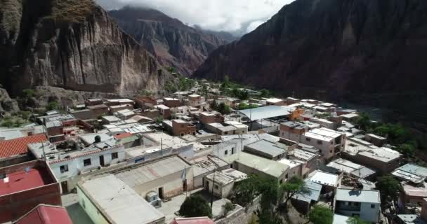 Aerial flying over Iruya, hidden town, at steep narrow valley surrounded of clouds, woods and dry colorful hills at background. Touristic town at Salta, Argentina — Stock Video
