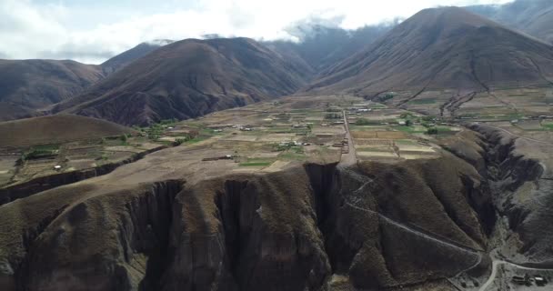 Antena general de cultivos agrícolas que cuelgan de la ladera de la montaña limitando hacia acantilado profundo. Nubes y cadena de alta montaña en el fondo. Pueblo Viejo, Salta, Argentina — Vídeos de Stock