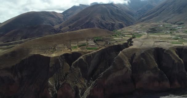 Flyg flygande mot gårdar grödor hängande från bergssluttningen begränsar mot djupa klippan. Moln och hög bergskedja i bakgrunden. Pueblo Viejo, salta, Argentina — Stockvideo