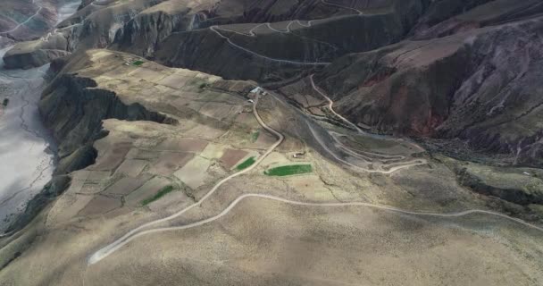 Escena aérea de drones de la agricultura local que cuelga de los acantilados de las montañas y la sinuosa pendiente ascendente de la carretera de grava. Pueblo Viejo, Iruya, Salta, Argentina — Vídeos de Stock