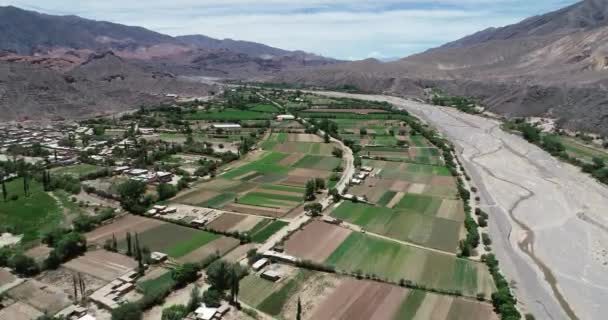 Εναέρια αεροκατευθυνόμενα σκηνή της μικρής τοπικής γεωργίας στην κοιλάδα του ποταμού σε ακερτικό τοπίο. Πράσινη κοιλάδα που περιβάλλεται από ξηρή πολύχρωμη ορεινή αλυσίδα. Paleta del Pintor, Μαϊμάρα, Χουτζουί, Αργεντινή — Αρχείο Βίντεο