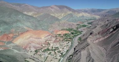 Vadi boyunca seyahat hava drone sahne renk dolu aşınmış dağlarla çevrili köyün panoramik manzarasını gösterir. Yedi renk dağlar, Purmamarca kasaba, Jujuy, Arjantin. Turistik şehir