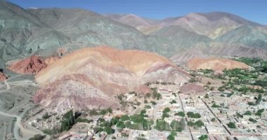 Geriye doğru hareket eden hava drone sahnesi, renkli kuru dağlarla çevrili köyün panoramik manzarasını gösteriyor. Yedi renk dağlar, Purmamarca kasaba Jujuy, Arjantin. Turistik bir şehir. Cerro siete renk