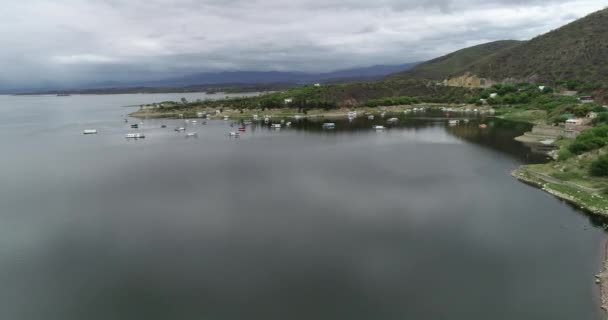 Escena aérea de drones volando sobre el lago hacia boyas de amarre y península turística. Montañas y bosques al fondo. Presa de Cabra Corral. Zona turística de Salta, Argentina — Vídeos de Stock