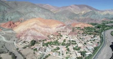 Geriye doğru hareket eden hava drone sahnesi, renkli kuru dağlarla çevrili köyün panoramik manzarasını gösteriyor. Yedi renk dağlar, Purmamarca kasaba Jujuy, Arjantin. Turistik bir şehir. Cerro siete renk